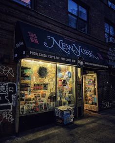 a store front with many items on display in the window at night, and graffiti all over the windows