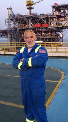 a man standing in front of an oil rig with his arms crossed and looking at the camera