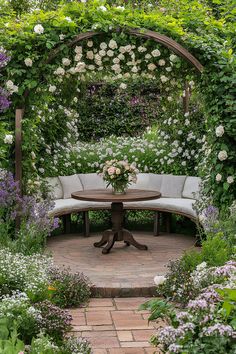 a bench and table in the middle of a garden with white flowers on either side