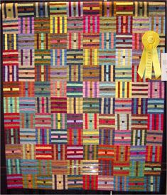 a colorful quilt with a yellow ribbon hanging from it's center and an award on the side