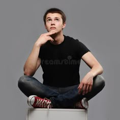 a young man sitting on top of a white box with his hand under his chin