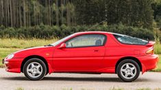 a red sports car is parked on the side of the road in front of some trees