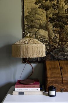 a lamp sitting on top of a white table next to a wall hanging with a tapestry