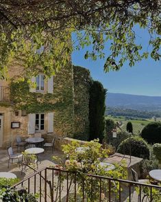 an outdoor patio with tables and chairs in front of a stone building surrounded by greenery