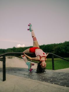 a woman doing a handstand on top of a skateboard in the park