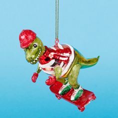 a glass ornament shaped like a dinosaur riding a skateboard on a blue background