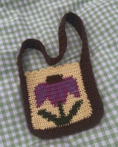 a crocheted bag with a purple flower on it sitting on a green and white checkered tablecloth