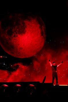 a man standing on top of a stage in front of a giant red ball with his arms up