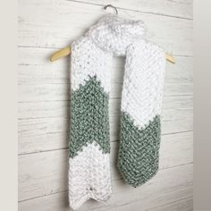 a crocheted scarf hanging on a wooden hanger next to a white wall