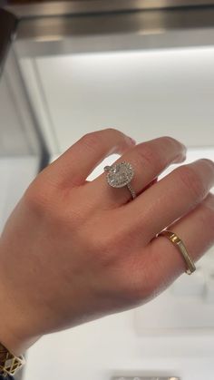 a woman's hand holding an engagement ring in front of a glass display case