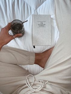 a person laying in bed with a book and cup