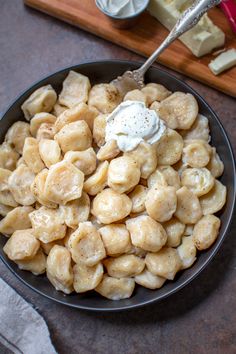 a bowl filled with dumplings and cream on top of a wooden cutting board next to cheese