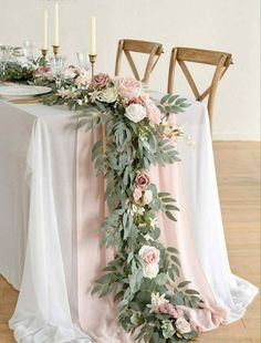 the table is decorated with pink flowers and greenery, along with candles on either side