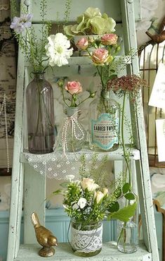 an old ladder is used as a shelf with flowers in jars and vases on it