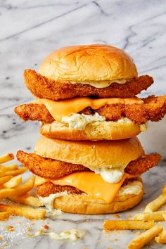 three chicken sandwiches stacked on top of each other with cheese and fries next to them