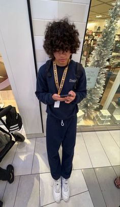 a young boy standing in front of a store looking at his cell phone while wearing sneakers