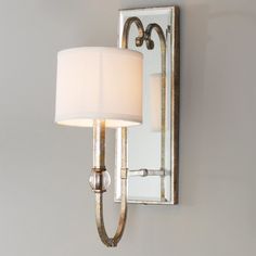 a wall light that has a white shade on it and is next to a mirror