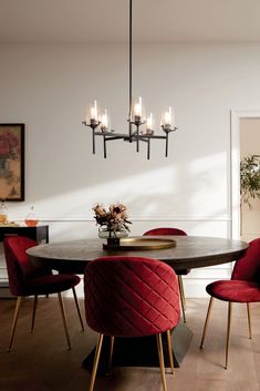 a dining room table with red chairs and a chandelier hanging from the ceiling