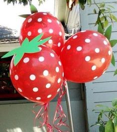 three red balloons with white polka dots and a green leaf on them are in front of a house