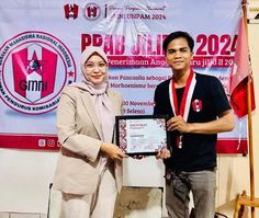 a man and woman standing next to each other in front of a banner holding an award