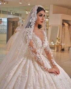 a woman in a wedding dress sitting on the floor wearing a veil and gown with flowers