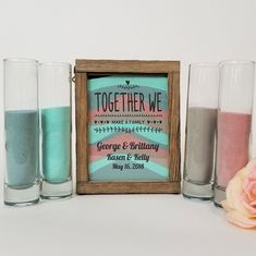 three shot glasses with sand in them next to a framed sign that says together we make family