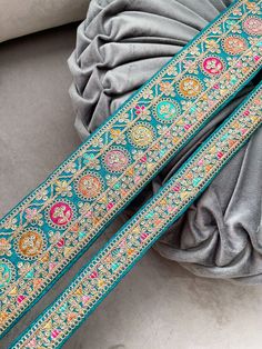 the pink and gold embroidered belt is laying on top of a gray pillow next to a grey t - shirt