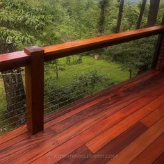 a wooden deck with metal railing and trees in the background