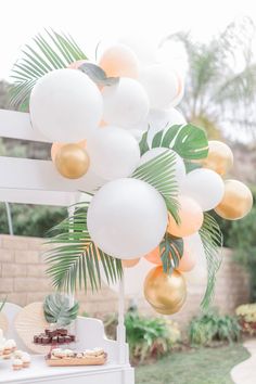 an outdoor party with balloons and desserts on the table, including palm leaf decorations