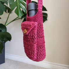 a pink crocheted bag hanging from a hook with a bottle in the pocket