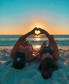 two people laying in the sand making a heart shape with their hands at the beach