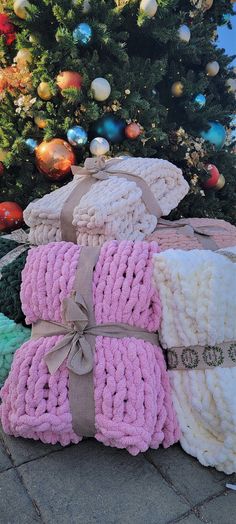 three knitted blankets stacked next to a christmas tree