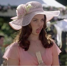 a woman in a pink dress and hat making a funny face with her tongue out