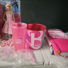 a barbie doll next to a pink car and other toys on a table with plastic wrap