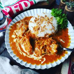 a white plate topped with meat and gravy next to rice on top of a table