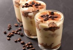 three glasses filled with dessert and coffee beans on top of a black table next to chocolate chips