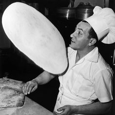 a black and white photo of a man in a kitchen holding a pizza dough disc