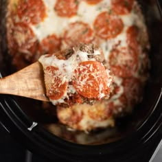 a close up of a wooden spoon in a slow cooker filled with meatballs and cheese