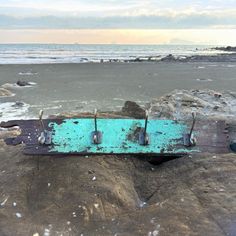 an old wooden board sitting on top of a rock next to the ocean and beach