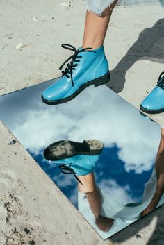 the reflection of a person's feet and shoes in a blue shoe mat on sand