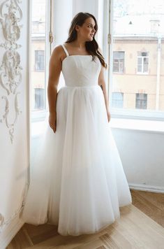 a woman standing in front of a window wearing a white dress