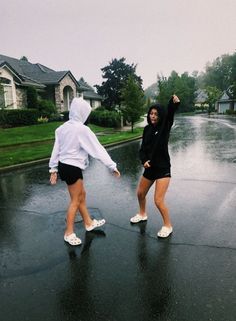 two girls are walking in the rain with their arms up and one girl is holding an umbrella