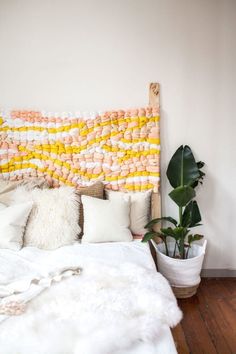 a white bed topped with lots of pillows next to a potted plant and a wooden headboard