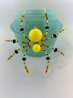 a yellow and black beaded spider sitting in front of a blue vase