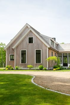 a house that is in the middle of some grass and gravel with a driveway leading up to it