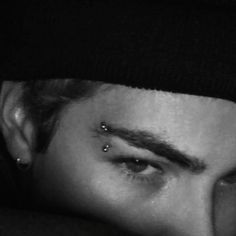 a man with piercings on his nose looking at the camera while wearing a beanie