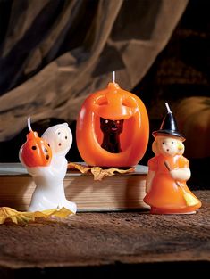 three halloween figurines sitting on top of an open book with pumpkins in the background