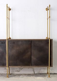 an iron and brass cabinet with two doors on the side, against a white wall