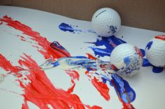 three golf balls sitting on top of a table covered in red, white and blue paint