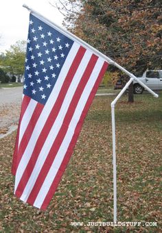 an american flag hanging from a white pole in the middle of a yard with leaves on the ground